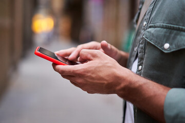 Close-up side view of the hands of an unrecognizable man holding and using a mobile phone outdoors scrolling and texting in social networks. Technology addiction.