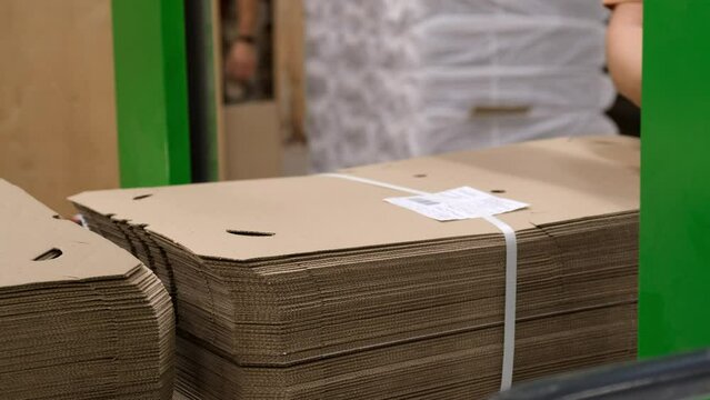 Finished product packaging line. An employee puts boxes into a flat mold and packs them with a plastic harness. A company producing cardboard containers.