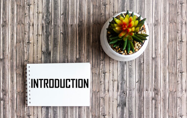 INTRODUCTION, text on a notepad on a wooden background next to a flower
