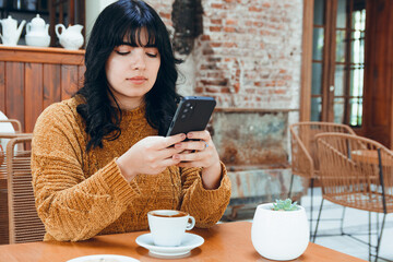 woman sitting in cafe sending messages on her mobile phone