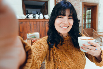 selfie photo of young latin woman with cup of coffee in her hand sitting happy and smiling