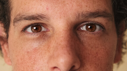 Detailed close-up shot of man's eye looking at the camera studio on beige background
