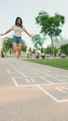 Joyful beautiful brunette girl dressed in casual clothes playing hopscotch game outdoors, having fun