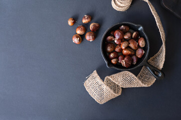 Traditional autumn and winter healthy nut treat, roasted chestnuts in pan and on black table background with copy space - obrazy, fototapety, plakaty