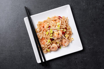 Pad Thai with shrimp and vegetables on black stone background. Top view