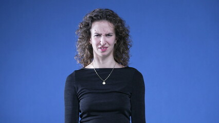 Woman reacting with disgust and dislike looking at camera while standing on blue background. Person...