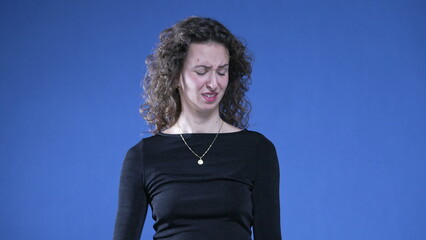 Woman showing revulsion to bad odor waving hand in disgust while standing on blue background and...