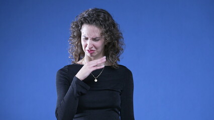 Woman showing revulsion to bad odor waving hand in disgust while standing on blue background and...