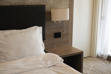 modern hotel room, bed with white linens and bedside table in a light stylish interior