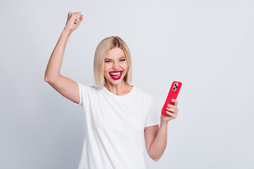 Photo of optimistic girl with bob hair dressed white t-shirt hold smartphone screaming win gambling...