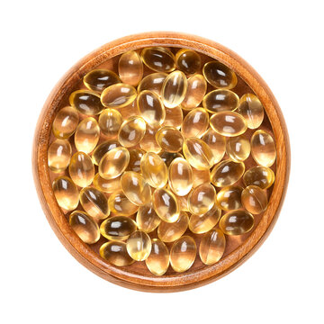 Soft gel capsules in a wooden bowl. Oral dosage medicine or dietary supplement in the form of a transparent capsule, consisting of a gelatin based shell surrounding a liquid fill of a certain dosage.