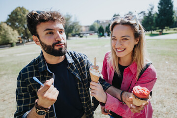 Caucasian friends enjoying ice cream in a city park on a sunny autumn day. They laugh and talk, carefree and relaxed, surrounded by nature's green environment.