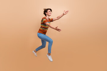Fototapeta na wymiar Full length profile photo of excited cheerful person jump rush arms catch empty space isolated on beige color background