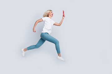 Full size photo of cheerful woman dressed white t-shirt denim pants fast run look at smartphone isolated on white color background