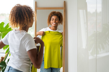 Cheerful african american woman trying on clothes and looking at the mirror