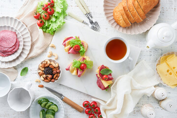 Preparation sandwiches snack for morning meal or breakfast on white marble background. Sandwiches with slice salami, cheddar cheese lettuce and tomatoes cherry on white marble background. Top view.