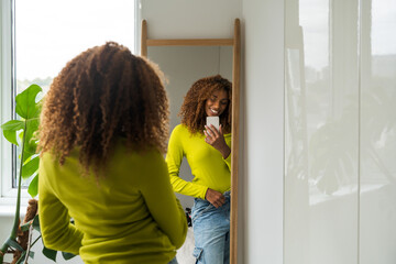 African american beautiful woman standing in front of the mirror and making smartphone photo