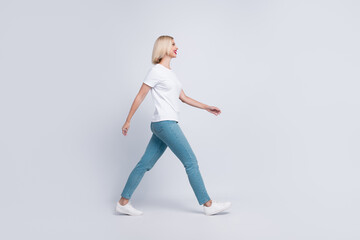 Full length photo of good mood gorgeous girl dressed white t-shirt denim pants walk look at empty space isolated on gray color background