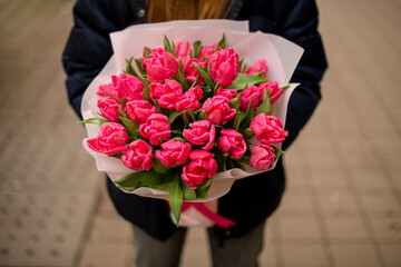 Girl in a black jacket standing on a city street with a bouquet of pink flowers