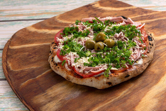 Individual homemade Neapolitan type pizzas in a clay oven with mozzarella tomato arugula ham green olives on a wooden board