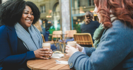 Young multiracial women having coffee break at vintage bar outdoor during winter time - Focus on african girl face