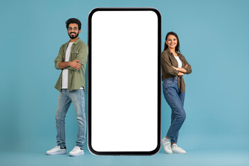 Positive young indian couple standing by big cell phone, mockup