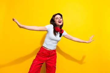 Photo of optimistic lovely woman dressed white t-shirt headphones on neck hold arms like wings isolated on yellow color background