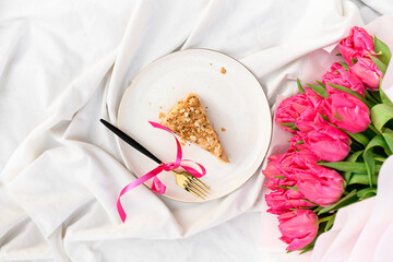 Pink tulips and a piece of Napoleon cake on a white porcelain plate