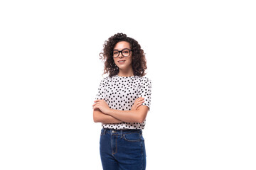 a slender young stylish woman with a curly haircut dressed in a blouse with polka dots wears glasses