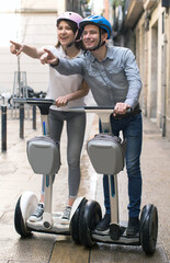 Fototapeta na wymiar Young couple guy and girl walking on segway in streets of european city