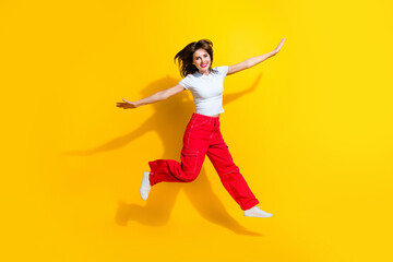 Fototapeta na wymiar Full length photo of cool carefree lady wear white t-shirt jumping high flying arms sides isolated yellow color background