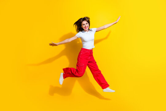 Full length photo of cool carefree lady wear white t-shirt jumping high flying arms sides isolated yellow color background