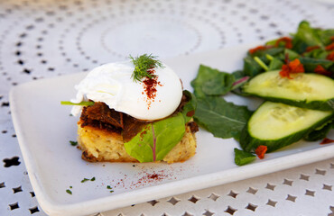 Healthy poached egg on top of potato kugel on white plate placed on patio table