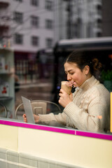 Girl with a dark hair in a light beige sweater with a glass of coffee
