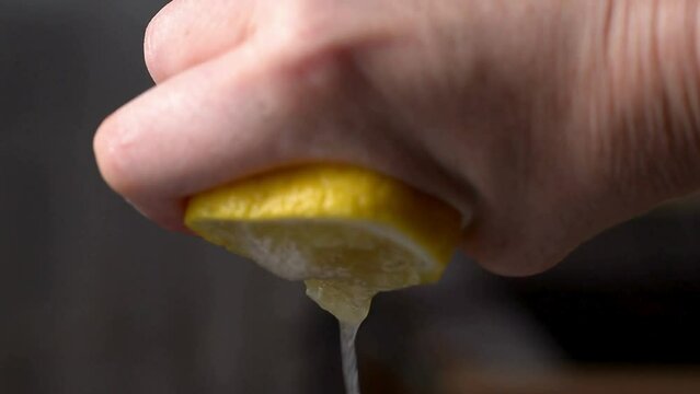 Closeup shot of person's hands squeezing lemon juice. Human squeezes half of lemon.