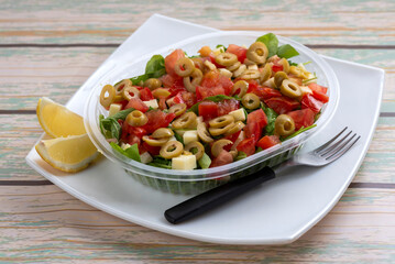 Vegetable salads with lettuce rice ham croutons tomato olives hard-boiled egg arugula carrot lemon cheese on a delivery tray on a white plate