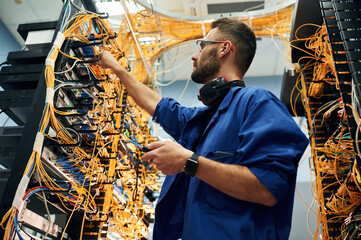Signal stability measured by device. Young man is working with internet equipment and wires in...