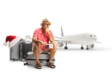 Mature male toruist sitting on a suitcase and waiting for a delayed christmas flight in front of an...