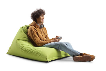 Guy sitting on a green bean bag armchair and playing a game with joystick © Ljupco Smokovski