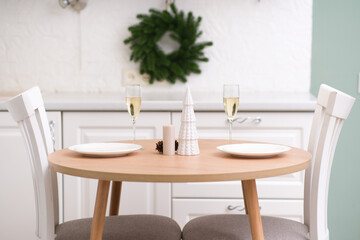 Two glasses of Champagne, two white plates on round wooden table. Christmas home interior. Ceramic vase with fir branches.