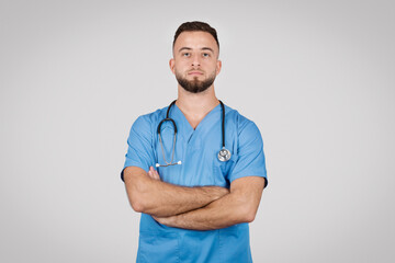 Confident male nurse in blue scrubs with arms crossed - obrazy, fototapety, plakaty