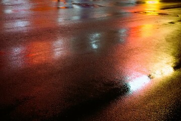 Nasse Straße mit bunter Lichterspiegelung in Stadt bei Regen, Kälte und Wind in der Nacht im...