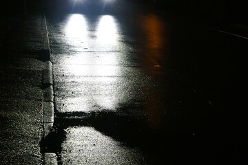 Gehweg und nasse Straße mit Auto und weißen Lichtern und Lichterspiegelung auf Straße bei Regen,...