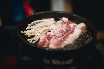 Cooking raw beef and golden needle mushroom on grilled meat on hot pan. Close up