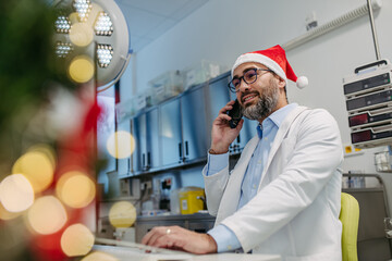 Portrait of doctor phone calling in emergency room, decorated for Christmas. Mature male doctor...