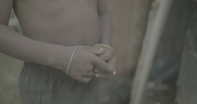 Black Boy without Shirt is Playing with Rubber Bands with his Hands