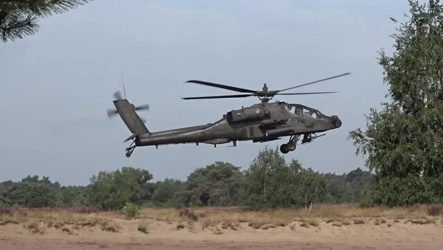 Military Helicopter hovering flying low over the ground between trees.
