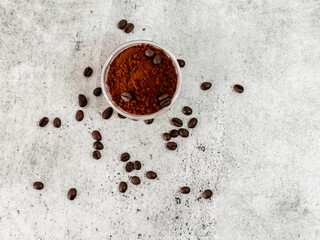 Top closeup shot of roasted coffee beans with defocused coffee powder in a glass bowl.