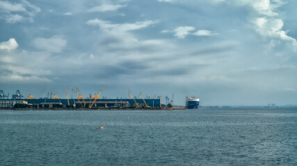 Fishings boat floats in the middle of the sea with a port and a large cargo ship in the background.