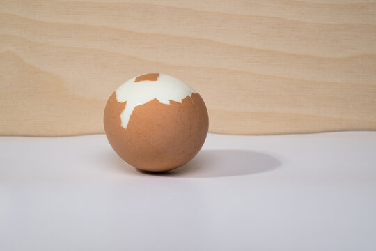 A brown partially peeled hard boiled egg against a background of white and wood